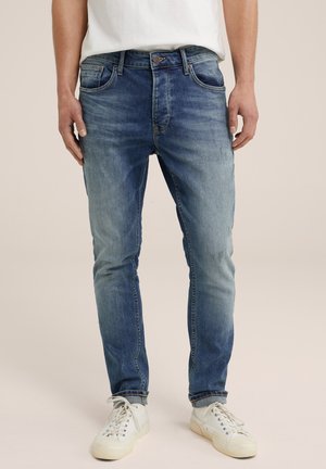 Light blue denim jeans with a faded finish, five-pocket design, and a slim fit, worn with white sneakers. Visible stitching and rivets.