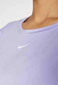 Světle fialové sportovní tričko s kulatým výstřihem, vyrobené z hladké látky, s malým bílým logem Nike v oblasti hrudi.