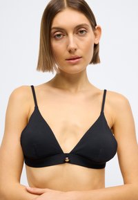 Μαύρο τριγωνικό bralette με υφή υφάσματος, λεπτές τιράντες και λεπτομέρεια με κουμπί σε χρυσό τόνο στο κέντρο μπροστά.