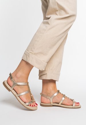 Gold strappy sandals with multiple straps, pearls on the center strap, and a flat sole, paired with light beige, ribbed cropped pants.