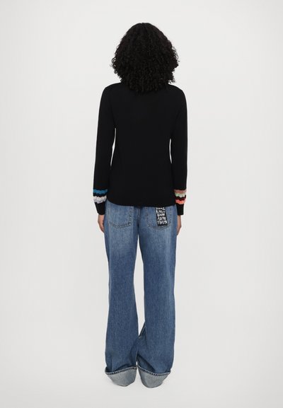 Svart langermet topp med fargerike ribbede mansjetter; kombinert med løse, lyse blå denimjeans med en dekorativ lommepatch.