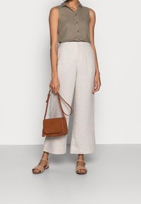 Blusa leggermente elastica senza maniche di colore verde oliva con bottoni, abbinata a pantaloni larghi in lino beige chiaro. Borsa a tracolla in pelle marrone e sandali.