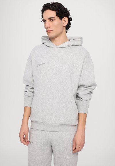 Grå hættetrøje lavet af blødt stof, med en stor hætte, lange ærmer og en lille trykt detalje på forsiden. Casual pasform og tekstur.