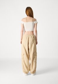 White cropped top with ruffled sleeves, paired with beige cargo pants featuring side pockets and elastic cuffs.