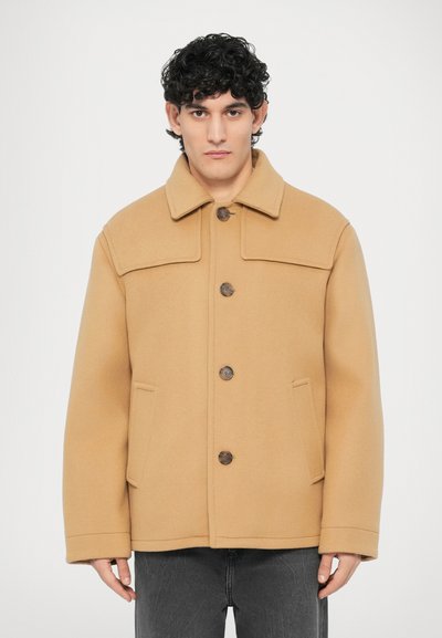 Veste beige en mélange de laine avec col, fermeture à boutons et deux poches avant. Présente une forme structurée et une texture lisse.