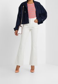 Chaqueta de mezclilla azul marino recortada, blusa a rayas rojas y blancas, jeans blancos de campana y tacones rosa empolvado. Texturas suaves y colores contrastantes.