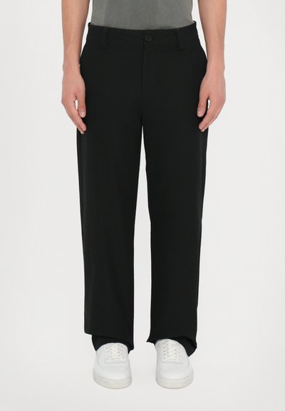 Pantalons larges noirs en tissu léger, dotés de passants de ceinture, d'un bouton à l'avant et de poches latérales. Associés à des baskets blanches.