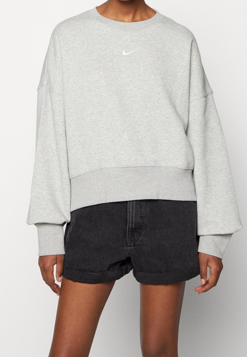 Sudadera gris con cuello redondeado, hombros caídos y dobladillo acanalado. Presenta un pequeño logo blanco de Nike en el pecho.