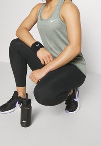 Šedý sportovní top Nike, černé legíny, černé tenisky s fialovými detaily, černá lahev na vodu s bílým logem, texturovaný náramek.