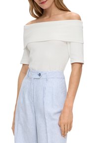 Haut blanc à épaules dénudées avec une texture lisse et une coupe ajustée. Associé à un pantalon taille haute rayé bleu et blanc.