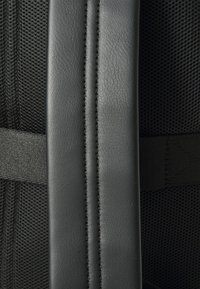 Primer plano de una correa acolchada negra con tela de malla texturizada y costuras reforzadas, probablemente parte de una mochila o bolsa.