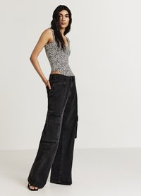 Pantaloni cargo neri con gambe larghe, dotati di grandi tasche laterali. Top senza maniche con un design a stampa animale in bianco e nero.