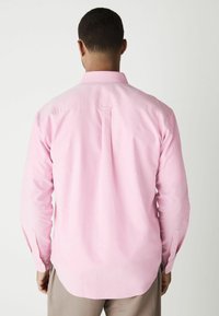 Rosa Hemd mit Knopfleiste und langen Ärmeln, mit Rückenschlitzdetails und Knopfmanschetten. Hergestellt aus einem glatten Stoff, mit einem klassischen Kragen.