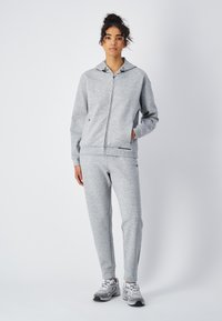 Felpa grigia con zip frontale e cappuccio regolabile, abbinata a pantaloni jogger grigi coordinati. Entrambi presentano un tessuto morbido e testurizzato.