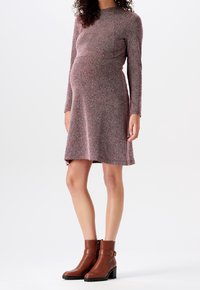 Schwangerschaftsabendkleid im Fischgrätmuster, mit langen Ärmeln, knielang und figurbetont. Braune Leder-Ankle-Boots mit Schnallenakzenten.