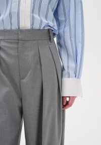 Hellblau gestreiftes Hemd mit weißem Kragen, kombiniert mit grauen plissierten Hosen, die eine glatte Textur und einen maßgeschneiderten Schnitt aufweisen.