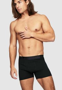 Svarta bomullboxerbriefs med en slät midja och utan synliga mönster. Modellen är poserad något på sidan för att visa passform och täckning.