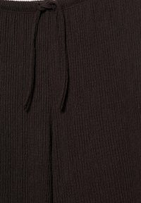 Zbliżenie na ciemnobrązową teksturowaną tkaninę z zawiązanym sznurkiem u góry, na środku.