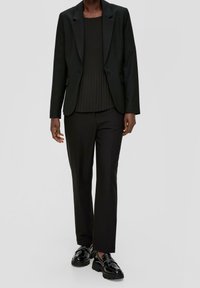 Svart kavaj med strukturerade axlar, enknapplåsning, matchad med en ribbad svart topp och svarta skräddarsydda byxor. Glansiga svarta loafers.