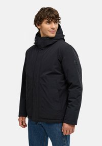 Zwarte geïsoleerde jas met capuchon, voorzien van een ritsluiting, twee voorkeurszakken en een textured stof. Eenvoudig ontwerp met minimale accenten.