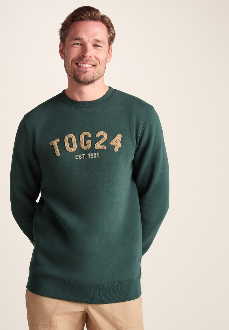 Green sweatshirt featuring textured gold lettering "TOG24 EST. 1958," with a crew neckline and ribbed cuffs and hem. Smooth cotton fabric.
