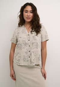 Hellbeige Kurzarm-Hemd mit Knöpfen, das ein schwarzes Linienstil-Muster von Gesichtern und floralen Designs zeigt, hergestellt aus einem strukturierten Leinenstoff.