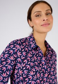 Camicia blu marina con motivo floreale a foglie in rosa e bianco. Presenta un colletto e una consistenza del tessuto liscia.