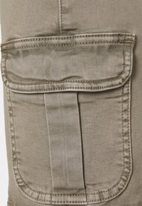 Detalle en primer plano de un bolsillo de pantalón cargo beige con tapa y costura vertical en una tela duradera.