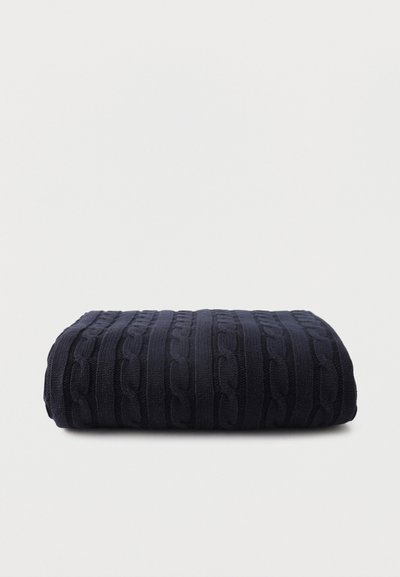 Pull en maille torsadée bleu marine foncé plié sur un fond clair uni.