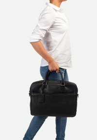 Schwarze Leder-Laptoptasche mit zwei oberen Griffen, glatter Textur, Fronttasche und Gepäckanhänger. Sie hat eine rechteckige Form und dezente Markenkennzeichnung.