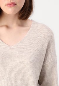 Beige ribbad stickad tröja med V-ringning och lös passform. Mjuk textur och något överdimensionerade ärmar. Minimalistisk design, utan mönster eller utsmyckningar.