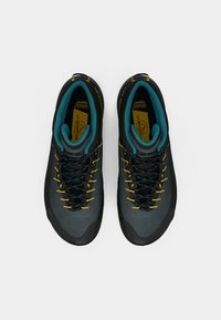 Melni un pelēki kāpšanas apavi ar tirkīza akcentiem, ar teksturētu virsmu, dzeltenām auklām, divām acīm un pastiprinātu pirkstu daļu.