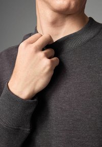 Gray sweatshirt with ribbed collar and cuffs, featuring a soft texture. A hand is adjusting the collar near the neckline.