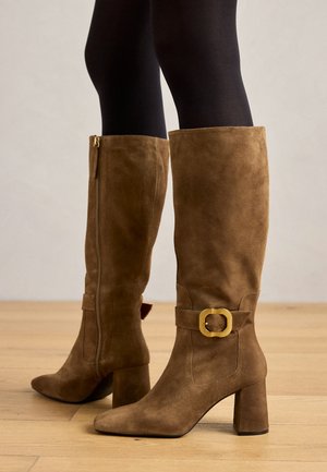 Bottes en suede marron jusqu'aux genoux avec une boucle carrée dorée, un talon épais et une pointe effilée, dotées d'une fermeture éclair sur le côté pour un enfilage facile.