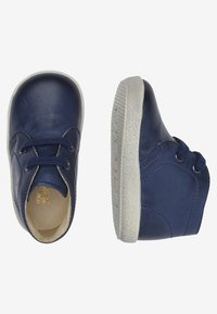 Botas de cuero azul marino con suelas de goma blanca, punta redonda, diseño con cordones, textura suave y detalles de costura en los laterales.