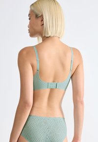 Mint green lace bra featuring a scalloped edge, adjustable straps, and back closure with hook-and-eye detail. Smooth textured fabric.