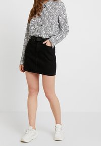 Svart denimminikjol med slim fit och framknäppning, kombinerad med en långärmad vit blus med ett svart spritts mönster.