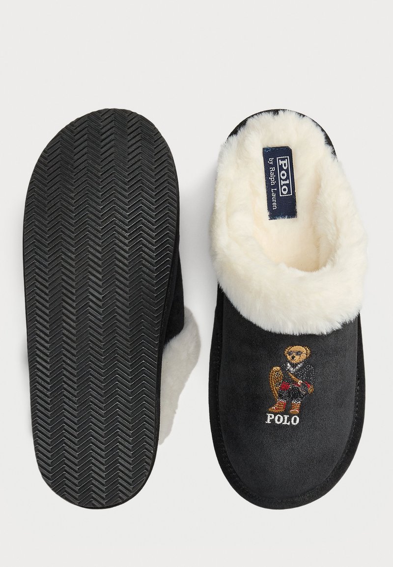 Chaussons en daim noir avec une doublure en shearling blanc. Ils présentent un logo d'ours brodé à l'avant et une semelle en caoutchouc noir texturé.