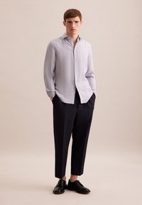 Camicia azzurra in lino con bottoni e colletto alla francese, abbinata a pantaloni blu scuro a vita alta e scarpe nere con lacci. Texture liscia.