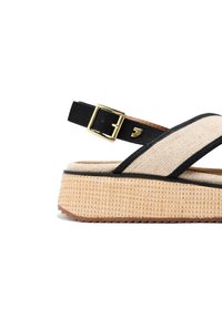 Sandalias de plataforma en negro y beige con parte superior de textil trenzado, correa ajustable con hebilla y suela de goma texturizada. Acento de herrajes dorados.