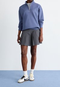 Ljusblå kvartslång ziptröja med Nike-logga, i kombination med en plisserad grå kjol och vita sneakers med svarta och gula accenter.