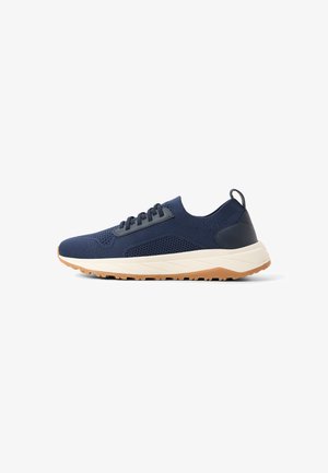 Sneaker in maglia blu navy con lacci neri, suola intermedia beige, suola esterna in gomma marrone e linguetta sul tallone, vista dal lato esterno.