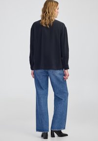 Maglietta nera a maniche lunghe con una texture liscia, abbinata a jeans in denim blu larghi. Stivali neri con tacco completano l'outfit.