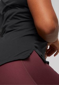 Svart atletisk topp med lös passform, med sidofickor. Matchad med vinröda texturerade tights. Mjukt tyg och släta sömmar synliga.