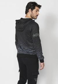 Čierna mikina s kapucňou a gradientným šedým dizajnom, obsahujúca šnúrkovú kapucňu a text "ENGINE" na rukáve. Hladká tkanina s rebrovanými manžetami.