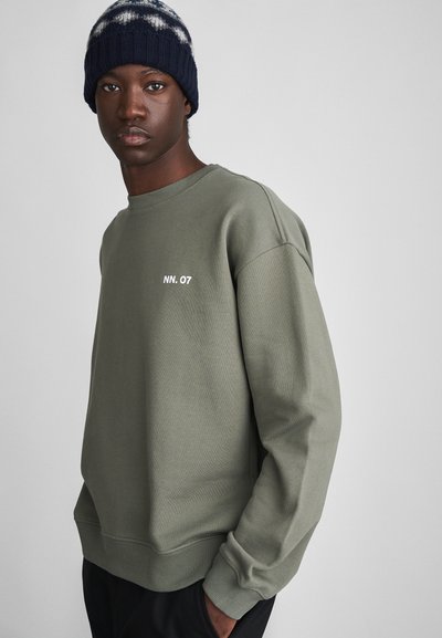 Sweatshirt vert olive avec un col rond côtelé, des épaules tombantes et le texte blanc "NN. 07" sur la poitrine. Tissu doux avec une coupe décontractée.