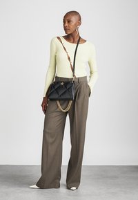 Must mustrilinega must käekott ketiga ja rihmaga, kombineeritud beige laiade pükstega ja heleda kollase tihedalt soojendava sviitriga.