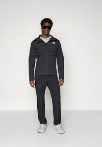 Črna izolirana jakna z zadrgo spredaj in kapuco, združena s hlačami v istem slogu. Oprema ima gladko teksturo in subtilno blagovno znamko.