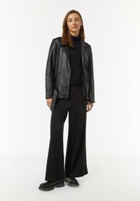 Schwarze Leder-Motorradjacke über einem schwarzen Rollkragenpullover, kombiniert mit weitem schwarzen Hosen und klobigen schwarzen Stiefeln. Minimalistisches Design.