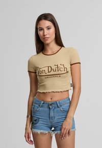 Bežkratka majica s kratkimi rokavi z rjavim obrobom, zlogom "Von Dutch" spredaj. Kombinirana z modrimi denim kratkimi hlačami s strganimi robovi in vezenimi detajli.